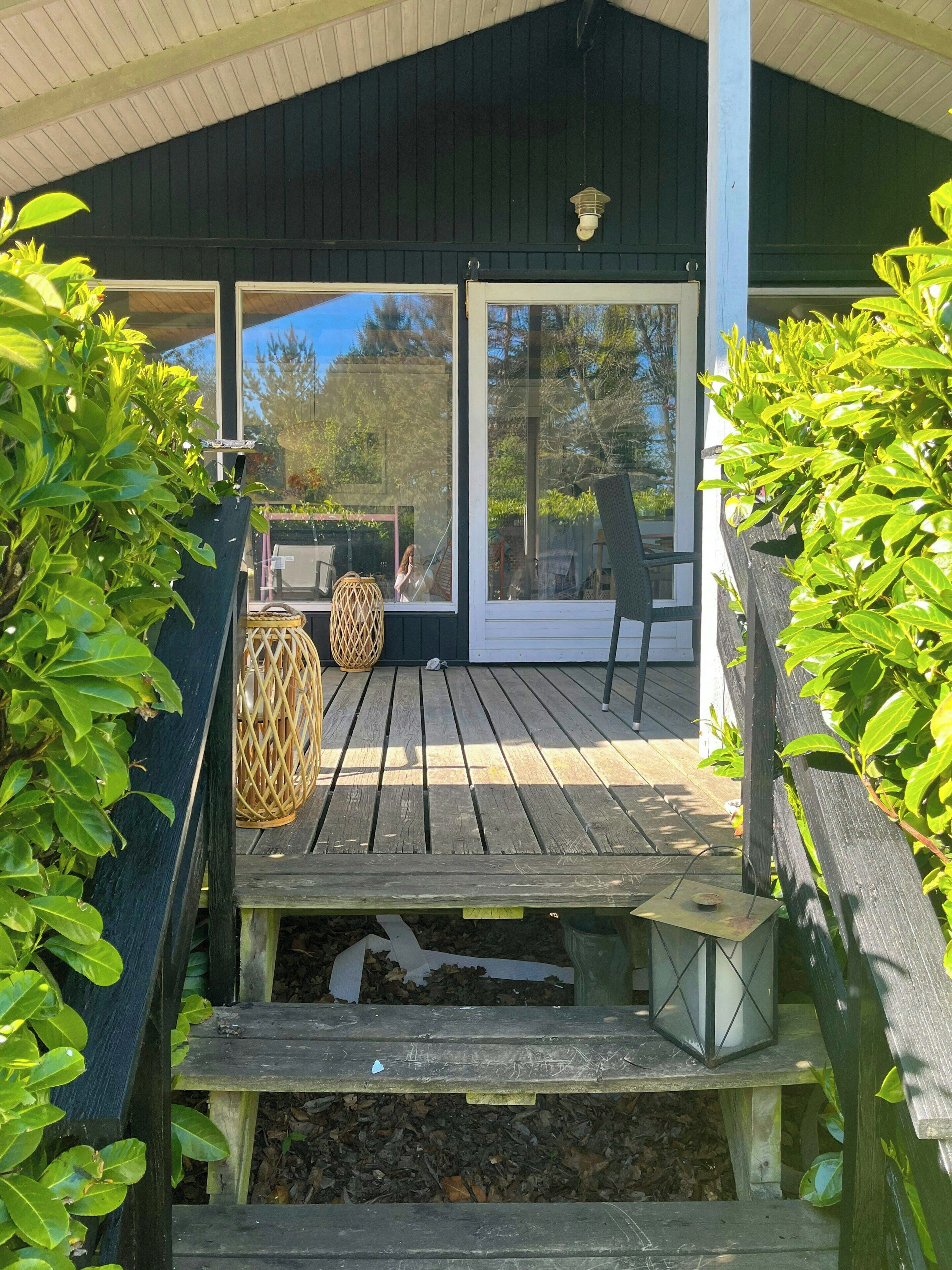 A wooden deck with a covered seating area, a wicker lantern, and a view of the outdoors.