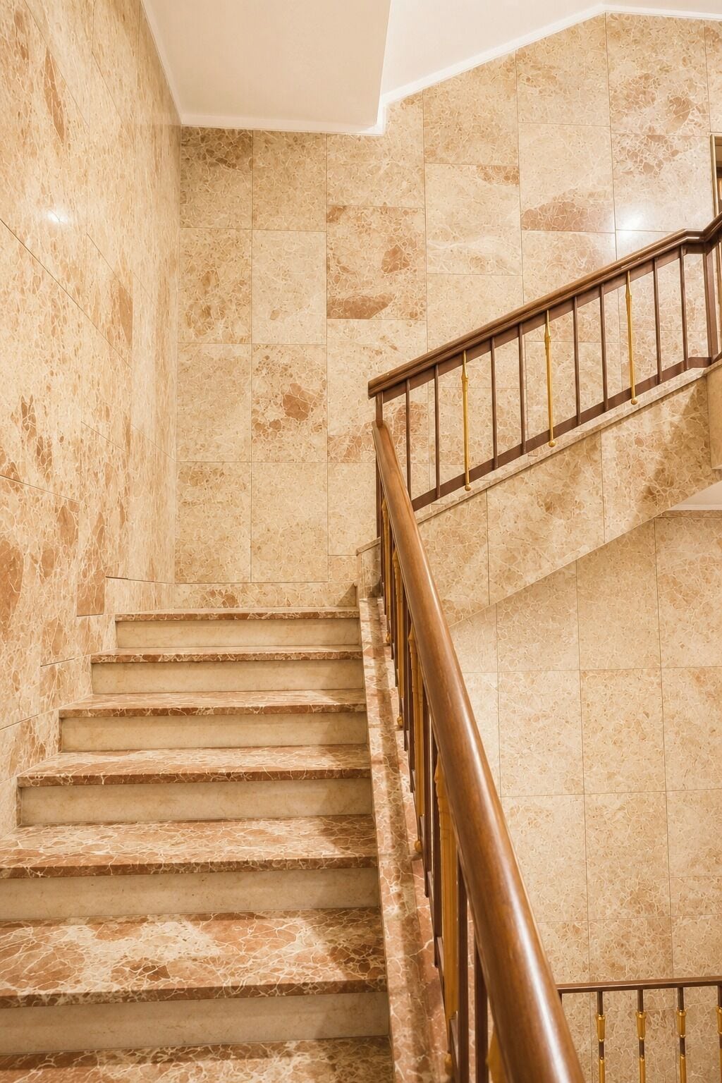 A marble staircase with a wooden handrail and a wall with a similar marble pattern.