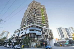 Ein modernes, hoch aufragendes Gebäude mit einer gewölbten Fassade, mehreren Balkonen und einem Glaszugang.