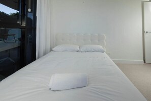 Ein Hotelzimmer mit einem großen Bett, einem weißen Kopfteil und Blick durch eine Glastür.