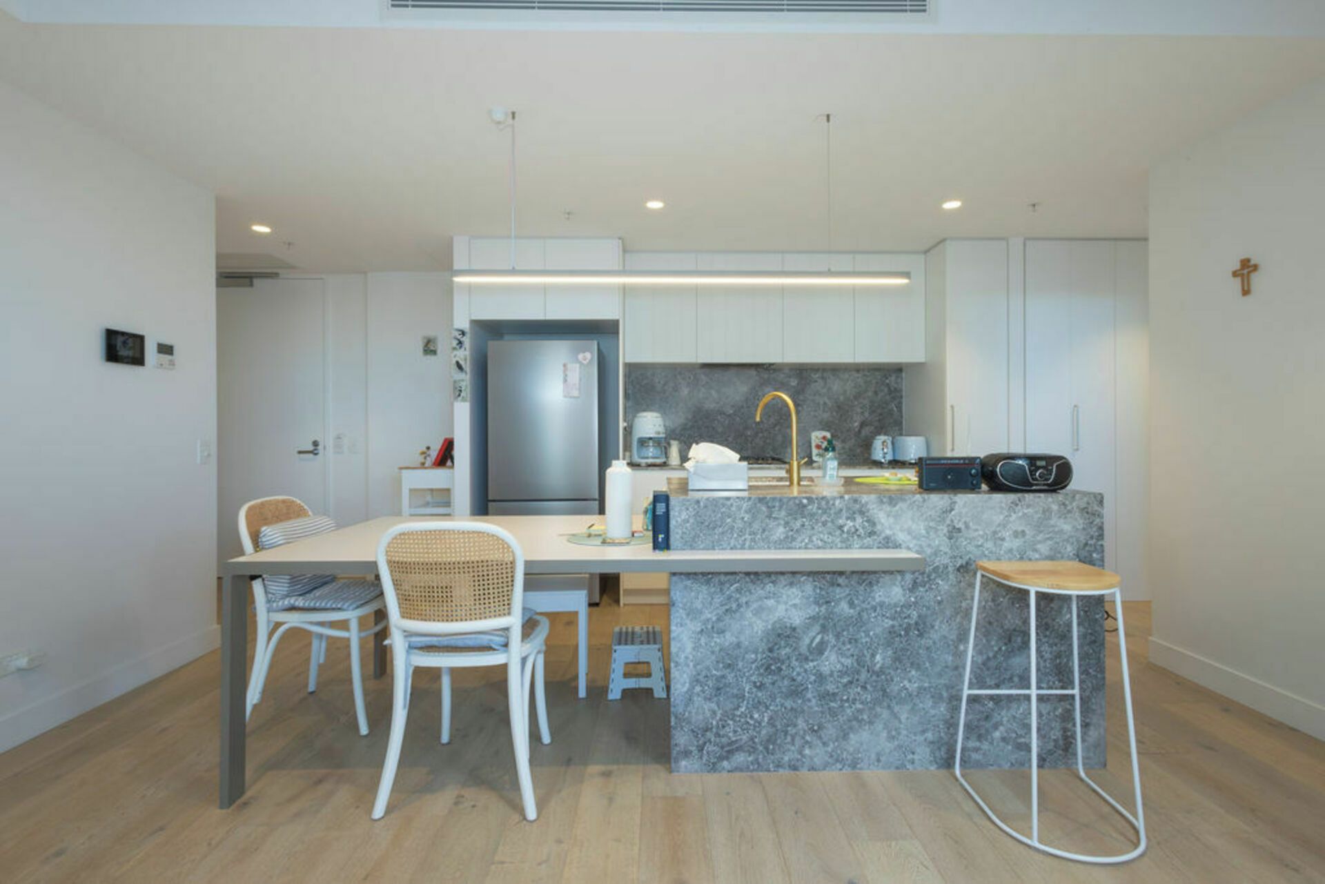 A modern kitchen with a marble countertop, stainless steel refrigerator, and white cabinetry.