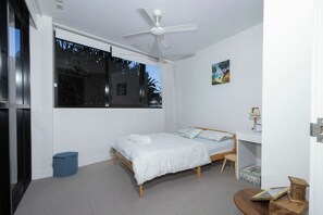 Een slaapkamer met een bed, een bureau, een stoel, een plafondventilator en een raam.