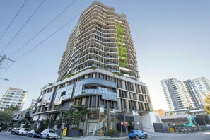 Ein modernes Hochhaus mit geschwungener Fassade, mehreren Balkonen und einer Mischung aus Glas- und Betonmaterialien.