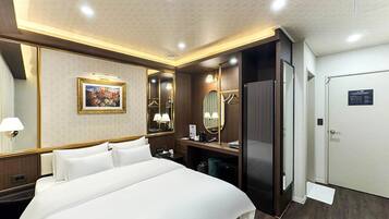 A hotel room with a bed, a desk, a mirror, a wardrobe, and a door.
