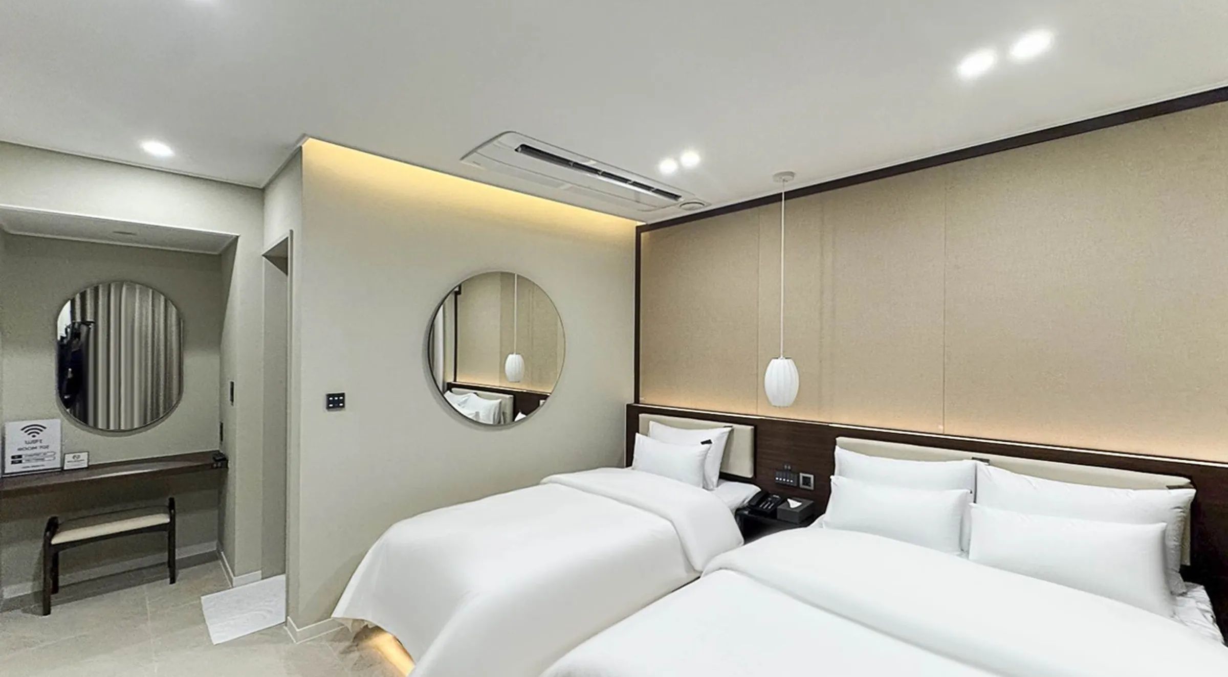 A hotel room with a bed, bedside table, mirror, and an air conditioning unit.