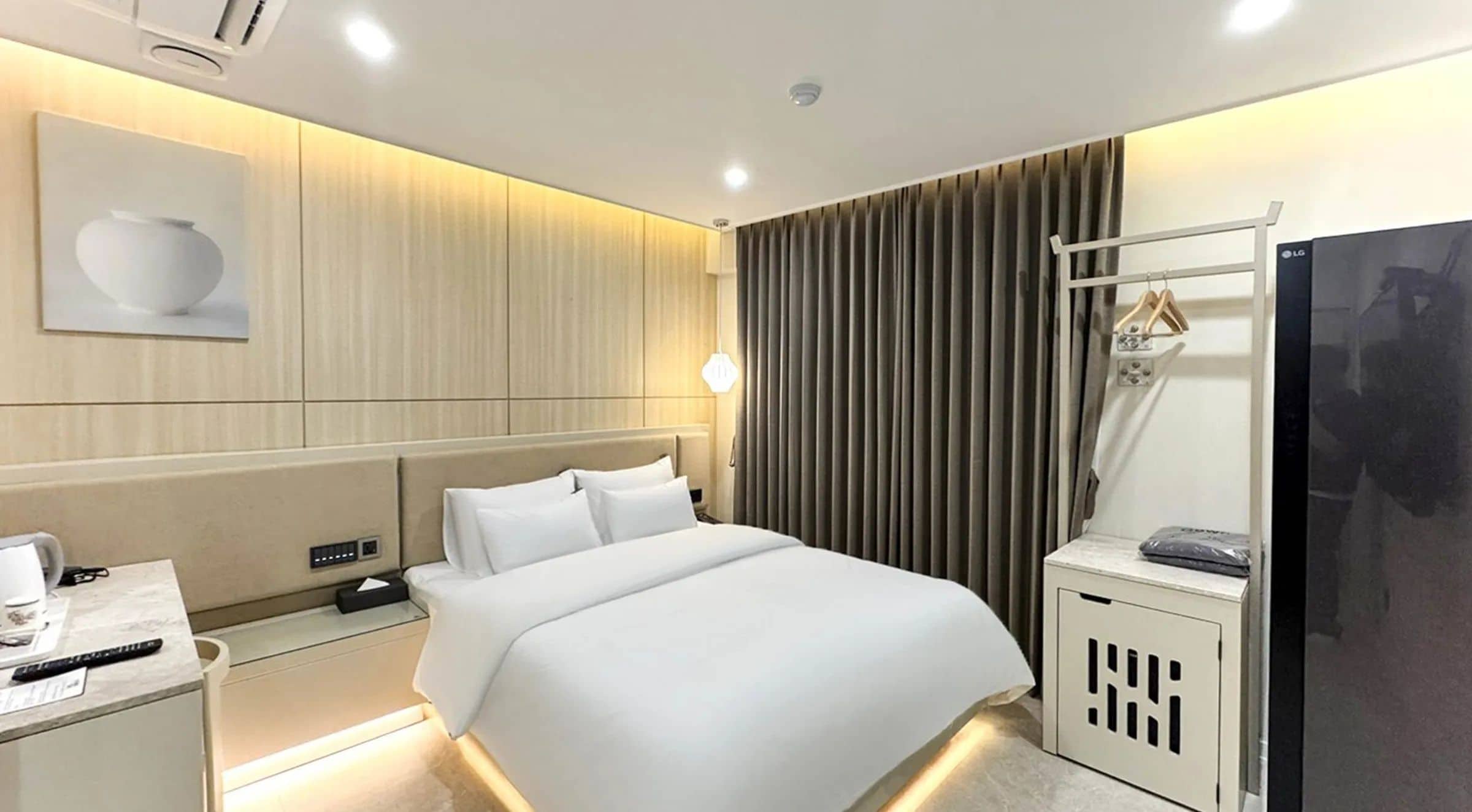Habitación de hotel con cama, mesita de noche, lámpara y armario.