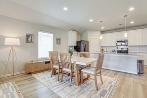 A modern kitchen with white cabinets, stainless steel appliances, and a dining area with wooden chairs and a white table. - Work & Explore! Sleek Richmond Home w/ Pool Access (Richmond)