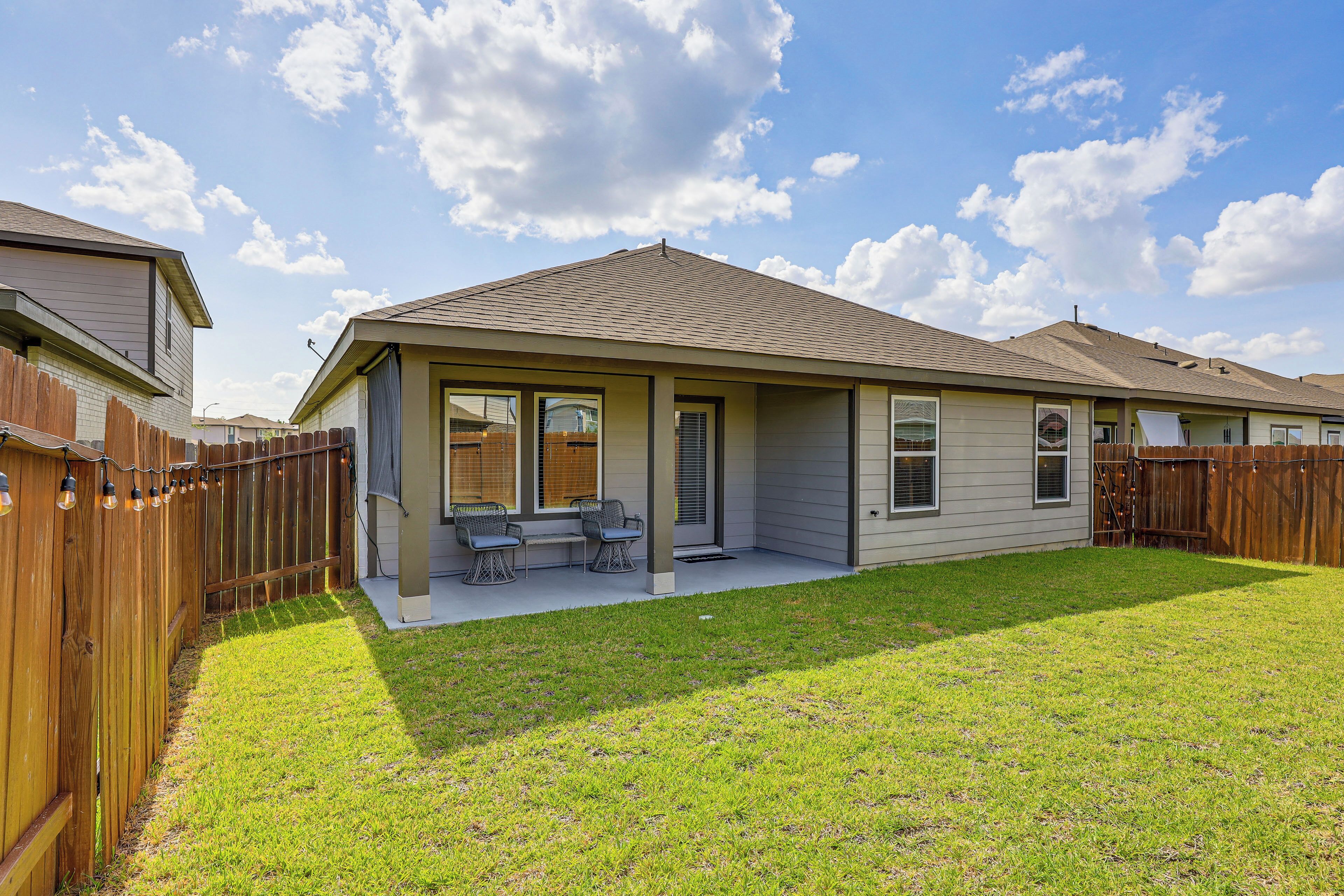 A residential house with a covered patio, a fenced yard, and a clear sky.