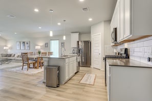 A modern kitchen with a central island, stainless steel appliances, and a dining area with a sofa and chairs. - Work & Explore! Sleek Richmond Home w/ Pool Access (Richmond)