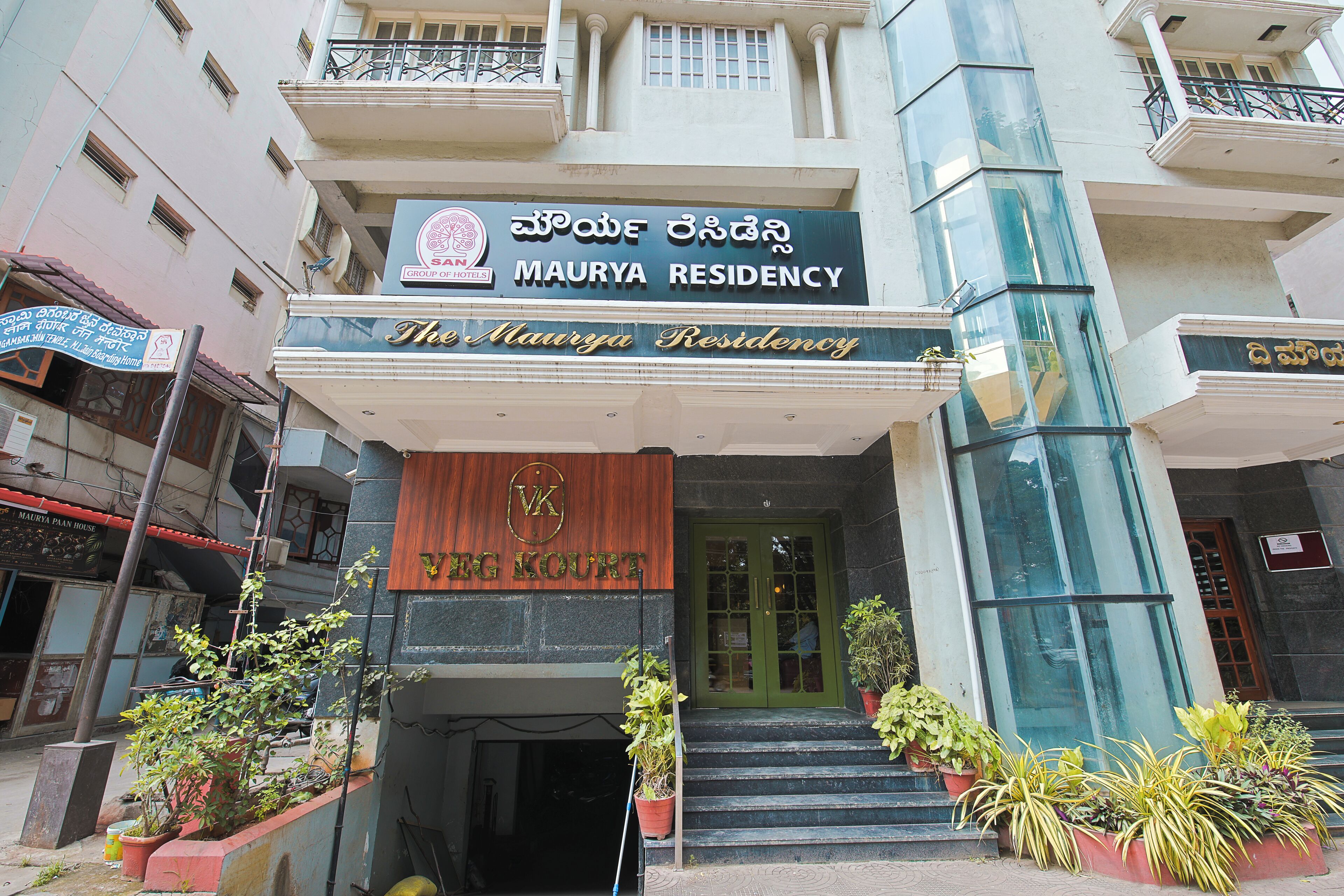 L’entrée d’un hôtel, avec une enseigne indiquant « Maurya Residency » et une plaque en bois indiquant « VG Kourt ».