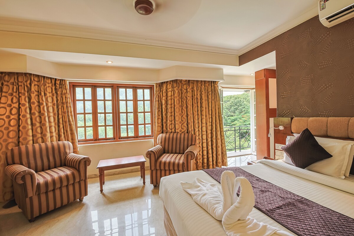 A hotel room with a bed, two armchairs, a small table, and a window with curtains.