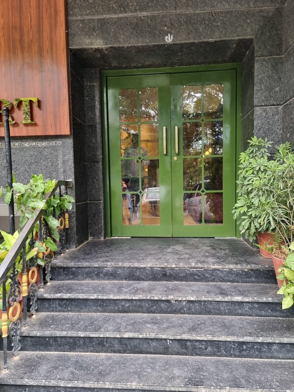 A staircase leading to a green door with a glass panel, surrounded by potted plants and a wooden panel on the left. - Hotel Maurya Residency (Mysore)