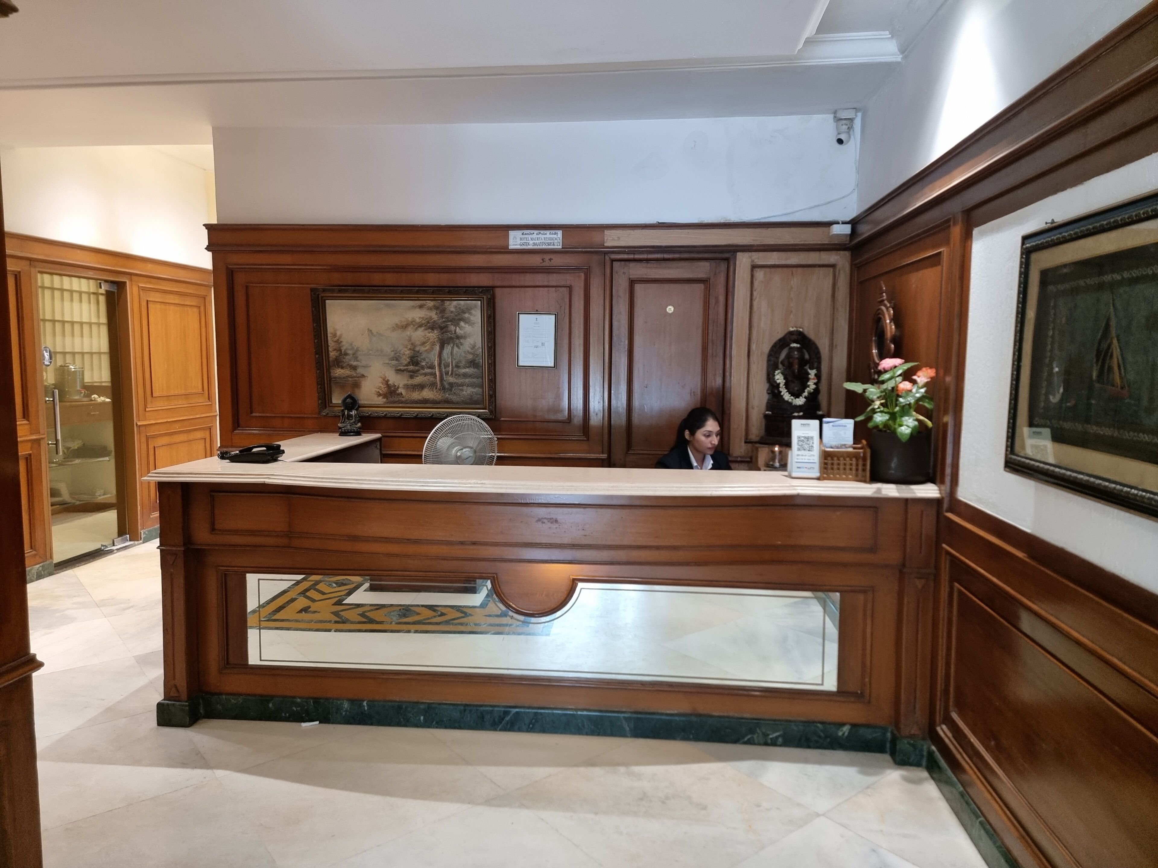 Un mostrador de recepción con incrustaciones de mármol, paneles de madera y un cuadro enmarcado en la parte superior.