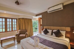 A hotel room with a bed, a chair, a window with curtains, and an air conditioning unit. - Hotel Maurya Residency (Mysore)