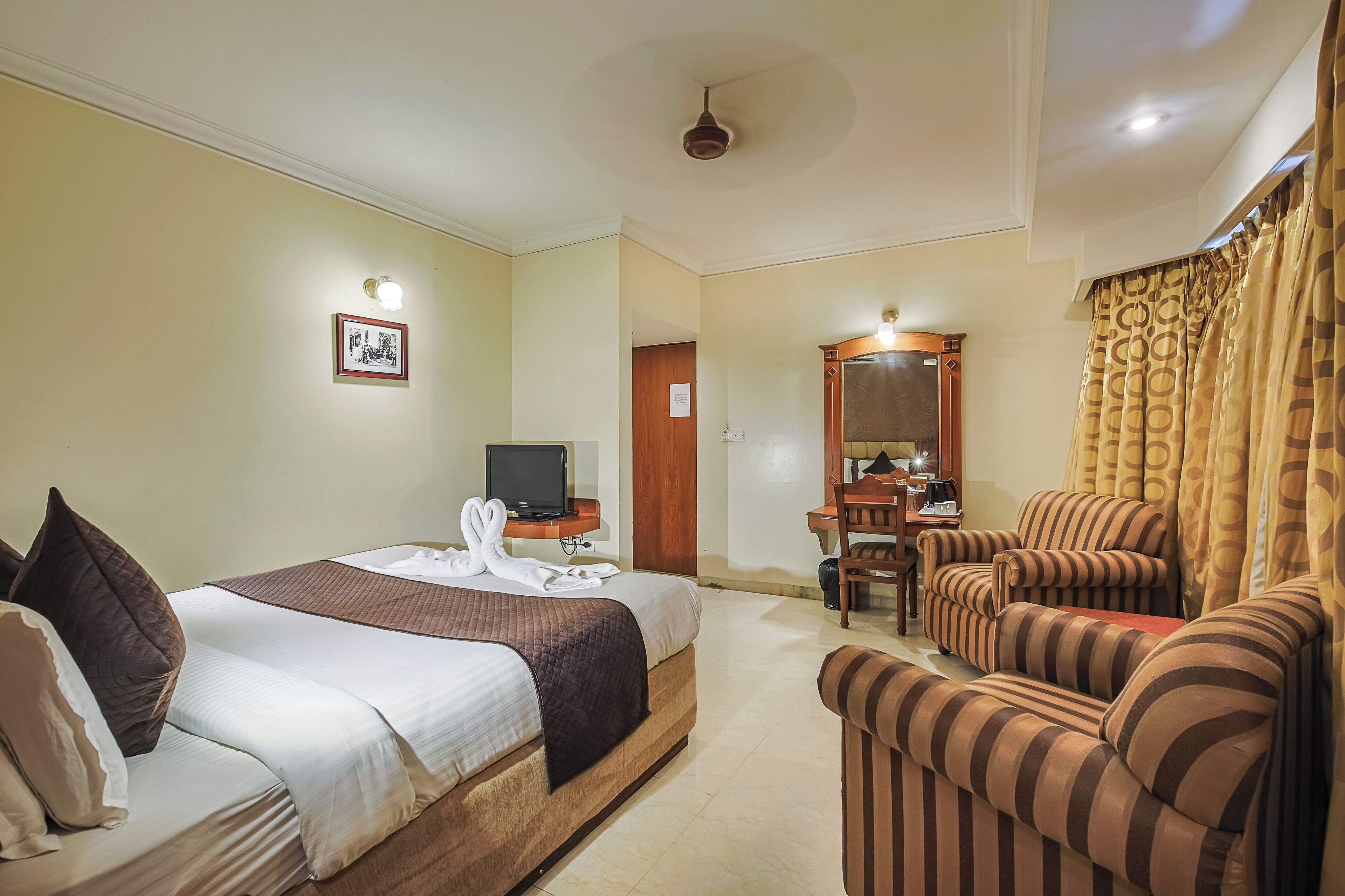 A hotel room with a bed, a television, a desk with a chair, and a sofa.