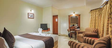 A hotel room with a bed, a television, a desk with a chair, and a sofa.