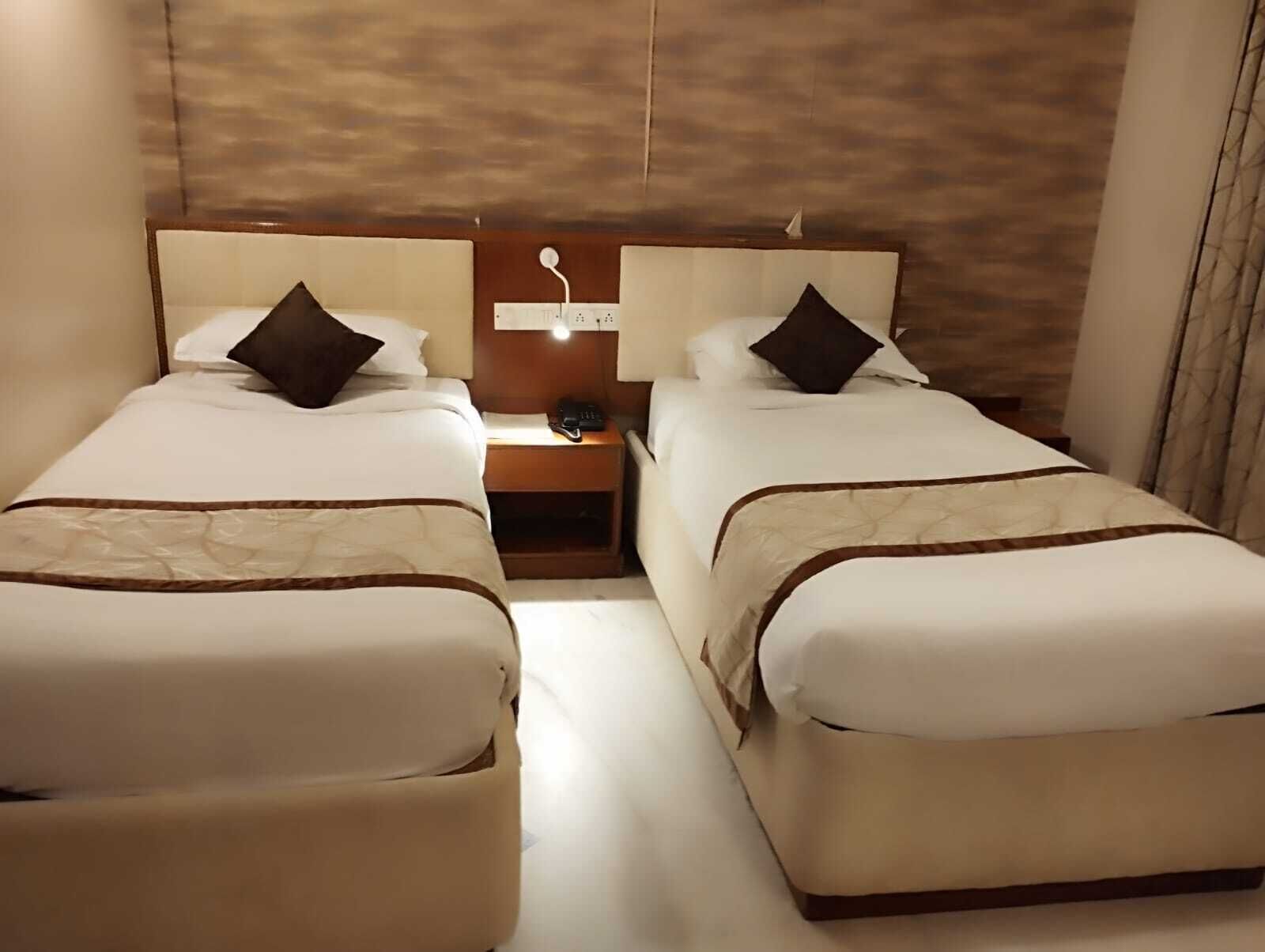 A hotel room with two beds, a nightstand, and a wall-mounted light fixture.