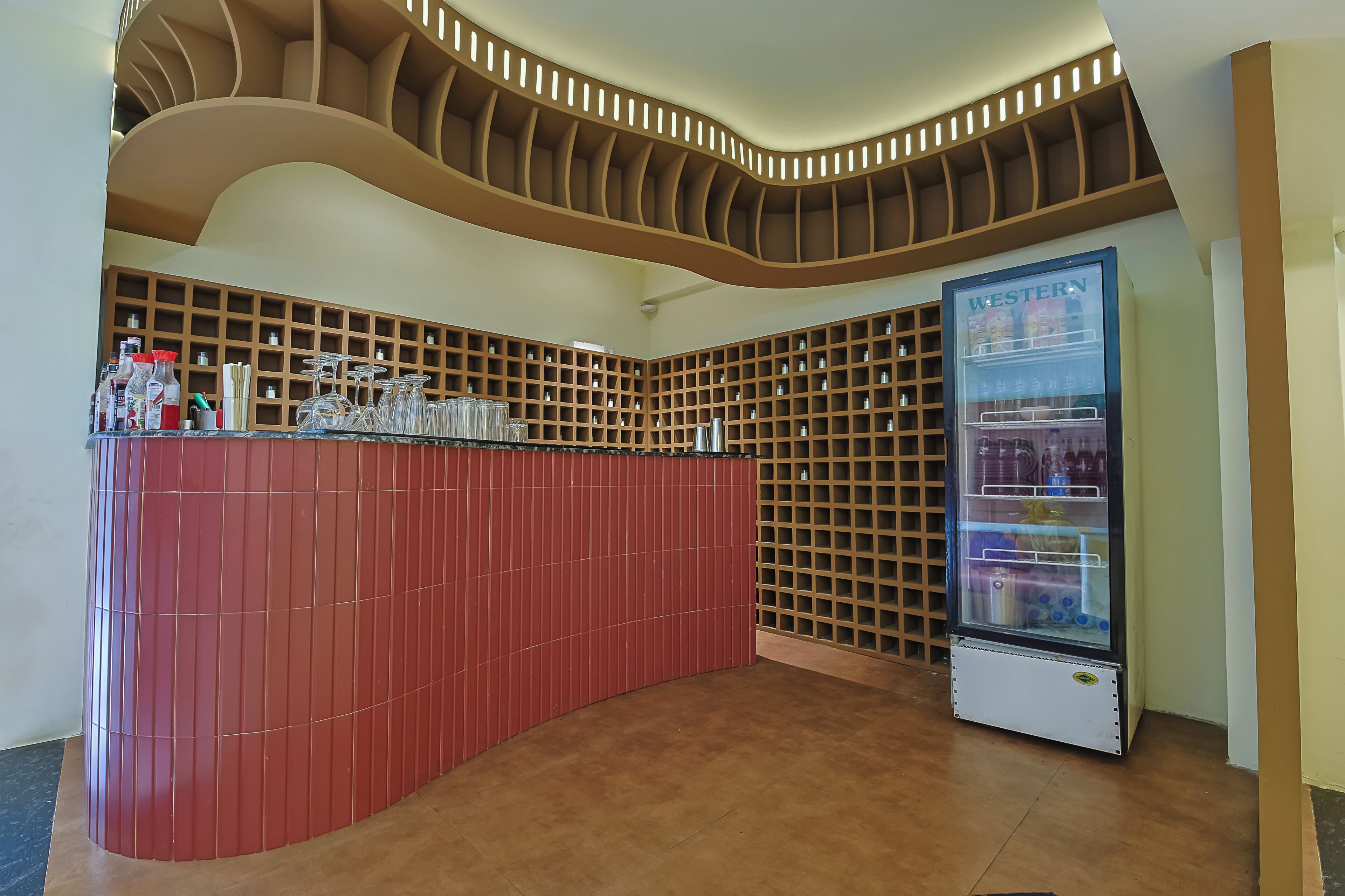 Un espace bar moderne doté d’un comptoir incurvé, d’un réfrigérateur à vin et d’un mur composé d’étagères.