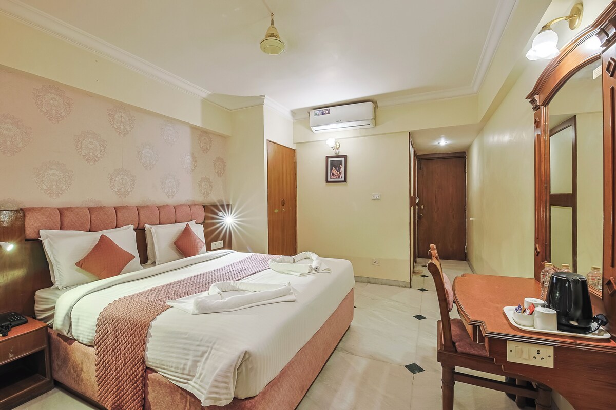 A hotel room with a bed, bedside table, mirror, and a desk with a coffee maker.