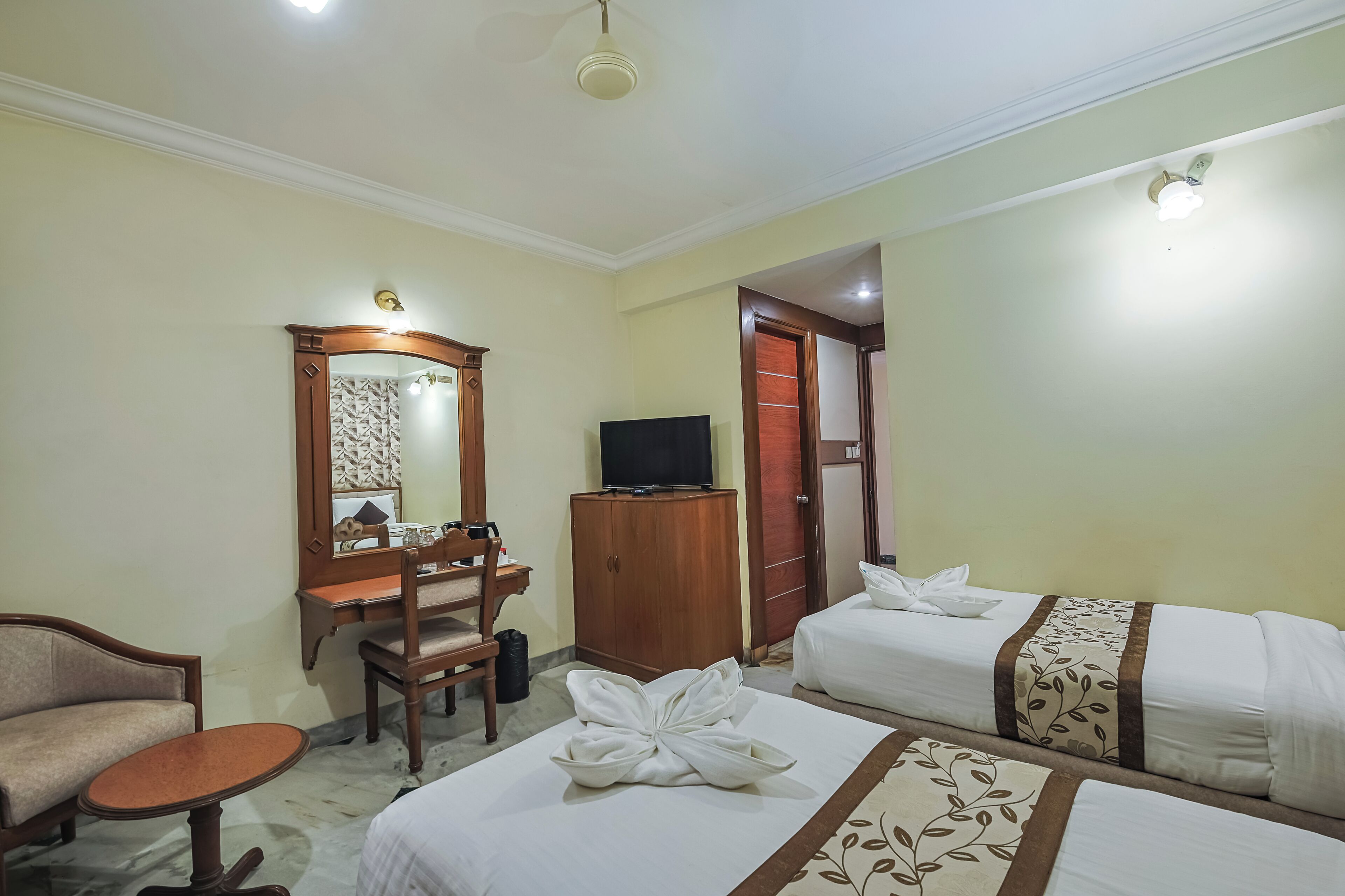 A hotel room with two beds, a desk, a chair, a television, and a wardrobe.