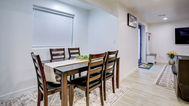 A dining area with a table set for four, flanked by wooden chairs, a window with blinds, and a television mounted on the wall. - Stay Near Salt Lake, Hill AFB & Snowbasin! (Layton)