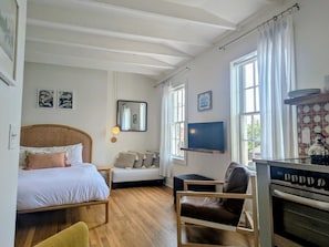 Ein Schlafzimmer mit einem Bett, einem Nachttisch, einem Sessel, einem Fernseher und einer Küchenzeile mit einem Herd.