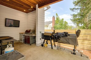 Une terrasse extérieure équipée d’un barbecue, d’une table et d’une bouteille de gaz.