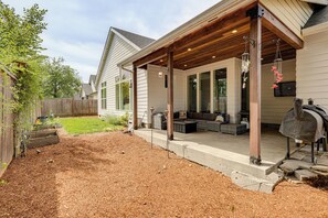 Ein überdachter Patio-Bereich mit Gartenmöbeln, einem Grill und einem gepflegten Garten.