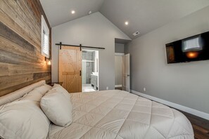 A bedroom with a bed, a TV mounted on the wall, and a wooden door. - Walk to Autzen Stadium: Eugene Getaway w/ Yard (Eugene)