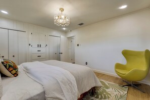A bedroom with a bed, a yellow chair, and a chandelier. - Furnished Patio & Spacious Yard! Seguin Escape (Seguin)