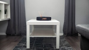A white table with a black object on top, a grey wall, and grey curtains. - The Lomond House (Balloch)