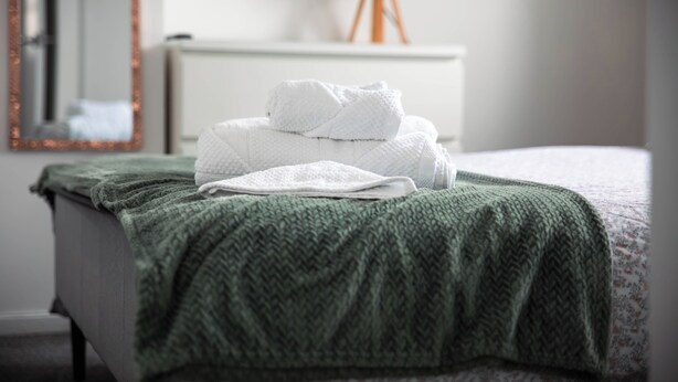 A neatly made bed with a green blanket and white towels. - The Lomond House (Balloch)