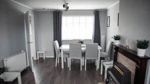 A dining area with a table and chairs, a radiator, a fireplace, and a window with curtains. - The Lomond House (Balloch)