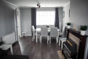 Uma área de refeições com mesa e cadeiras, um radiador, uma lareira e uma janela com cortinas.