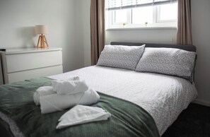 Een opgemaakt bed met een wit en groen dekbedovertrek, twee kussens en een gevouwen witte handdoek.