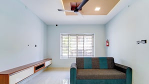 Une pièce avec un ventilateur de plafond, une fenêtre avec des stores, un extincteur, un canapé et un banc en bois.