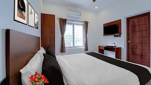 Une chambre d’hôtel avec un lit, un ventilateur de plafond, une fenêtre avec des rideaux, un téléviseur fixé au mur et une porte en bois.