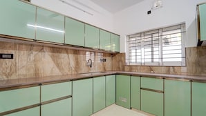 Une cuisine avec des meubles de couleur verte, un pare-feu en marbre et une fenêtre équipée de stores horizontaux.
