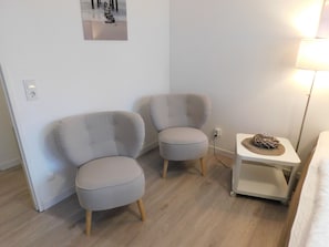 Una habitación con dos sillones grises, una mesita auxiliar blanca con una cesta tejida y una lámpara de pie.