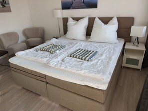 Ein ordentlich bezogenes Bett mit einem gestreiften Kopfkissen, einer Nachttischlampe und einem Nachttisch mit Schublade.