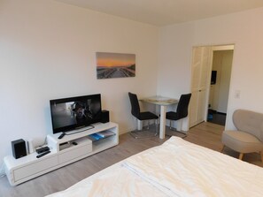 Ein Hotelzimmer mit einem Bett, einem Fernseher, einem Schreibtisch mit zwei Stühlen, einem Bild an der Wand und einer Tür zu einem weiteren Raum.
