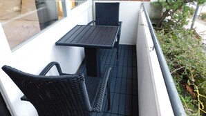 A balcony with a table and two chairs, a glass door, and a brick wall. - Cozy one-room apartment right on the market square and next to the spa gardens (Grömitz)