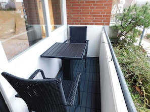 Ein Balkon mit Tisch und zwei Stühlen, einer Glastür und einer Ziegelwand.