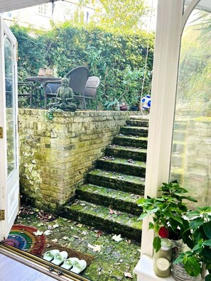 A staircase leading to a garden area with outdoor furniture and a statue. - Kensington Garden Sanctuary - birds, squirrels & unique art! By Holland Park (Greater London)