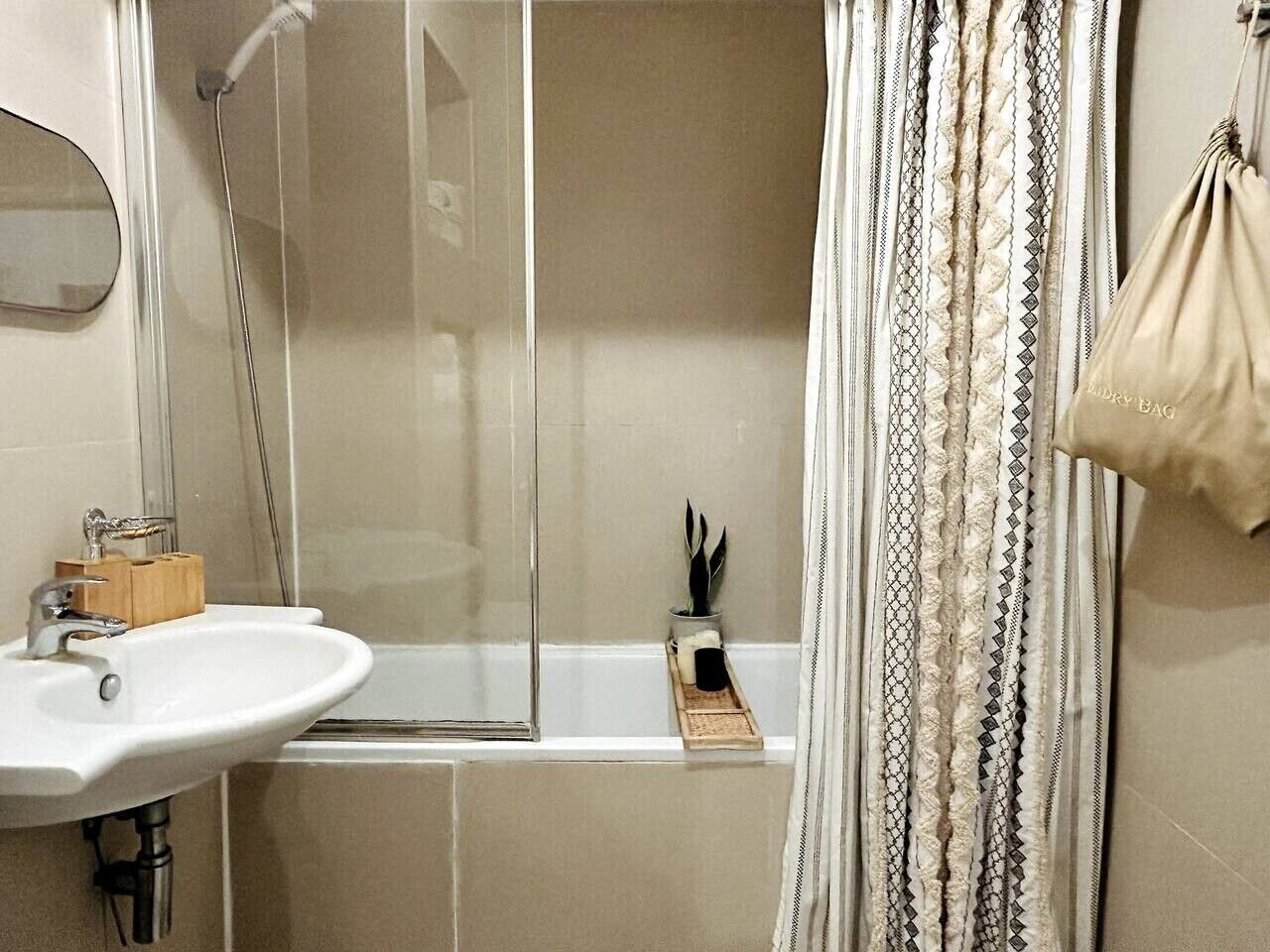 Um banheiro com chuveiro em box de vidro, pia com porta-sabonete de madeira e cortina estampada.