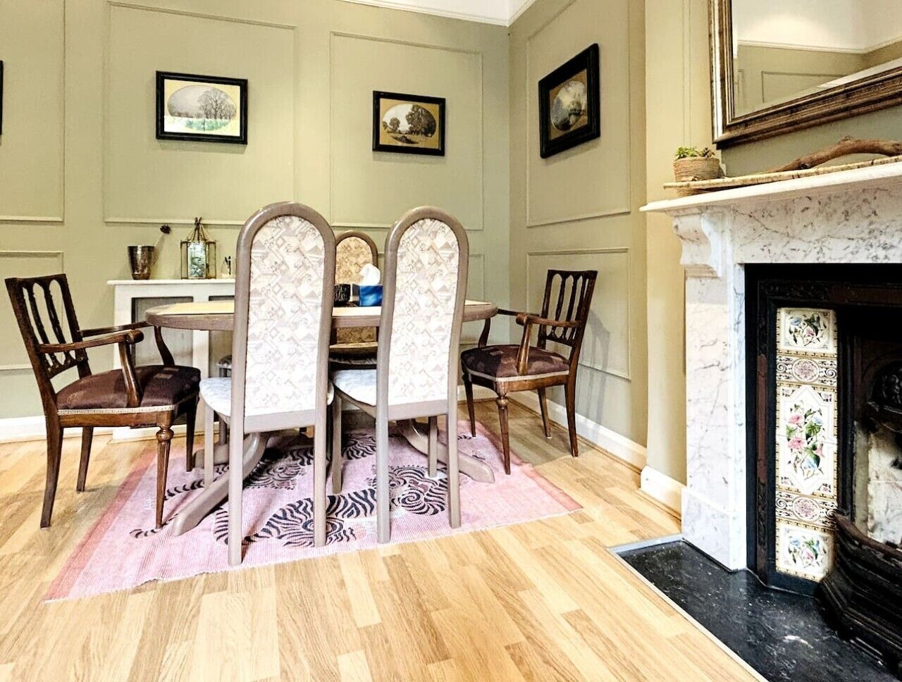 Uma sala de jantar com mesa e cadeiras de madeira, lareira e quadros nas paredes.