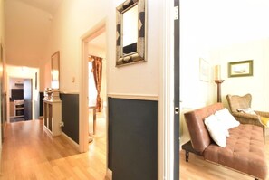 A hallway with a dark wall, a mirror, and a brown leather sofa with a cushion. - Kensington Deluxe Suite: 1-bedroom home in London - A Grand Stay (Greater London)