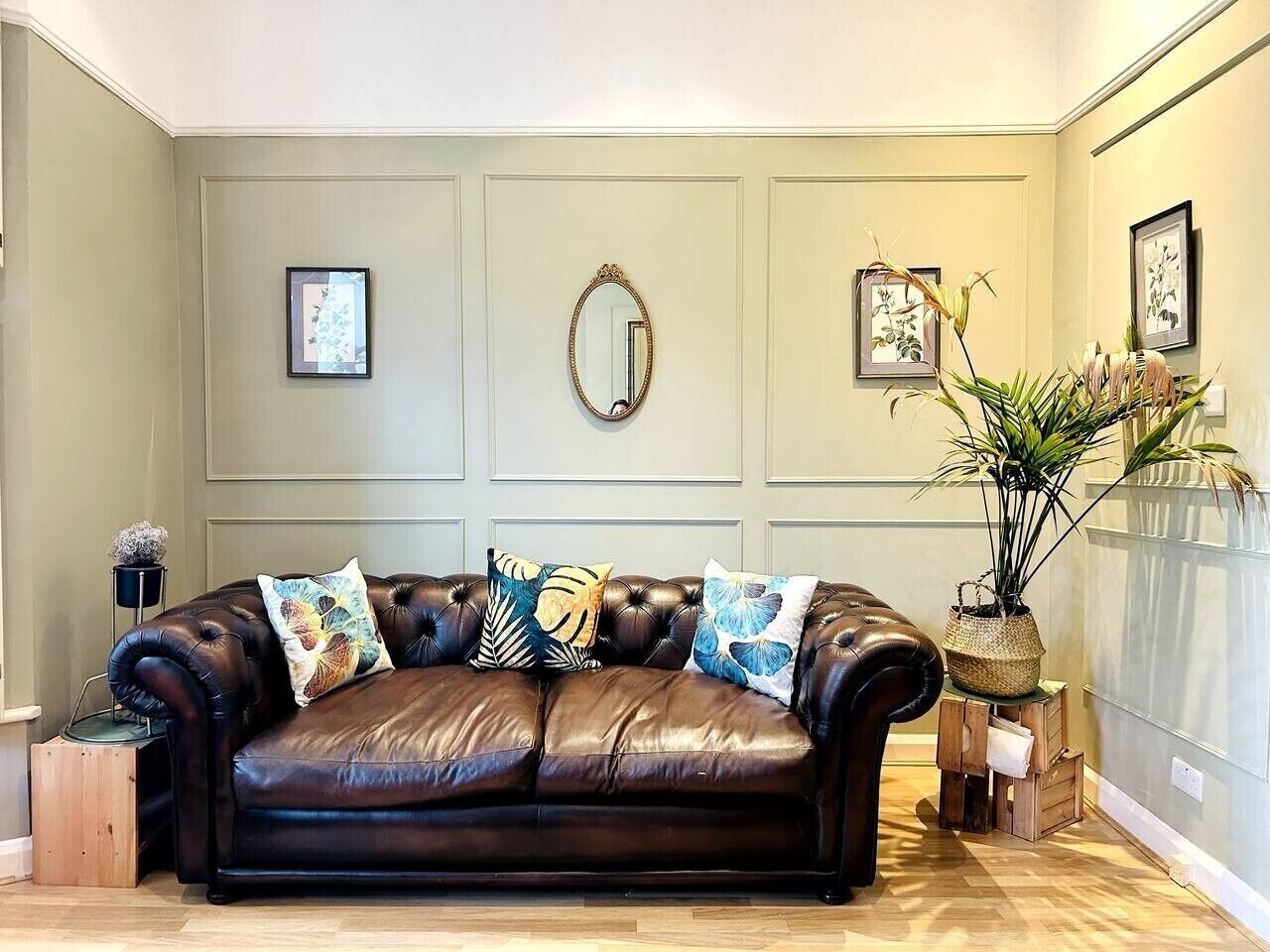 A brown leather sofa with patterned cushions, a mirror, framed artwork, and a potted plant in a corner.