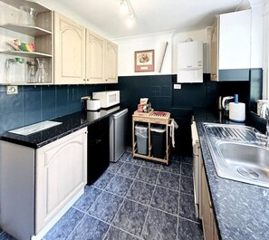 A compact kitchen with a microwave, sink, and a small trash bin. - Kensington Deluxe Suite: 1-bedroom home in London - A Grand Stay (Greater London)