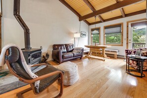 A cozy living room with a fireplace, leather sofa, wooden floor, and large windows. - Greek Peak Retreat! Townhome w/ Mountain Views (Cortland)